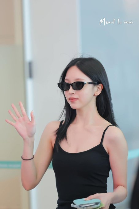 A young woman wearing black sunglasses and a black tank top waves while holding a phone, with the text 'Meant to me' visible at the top.