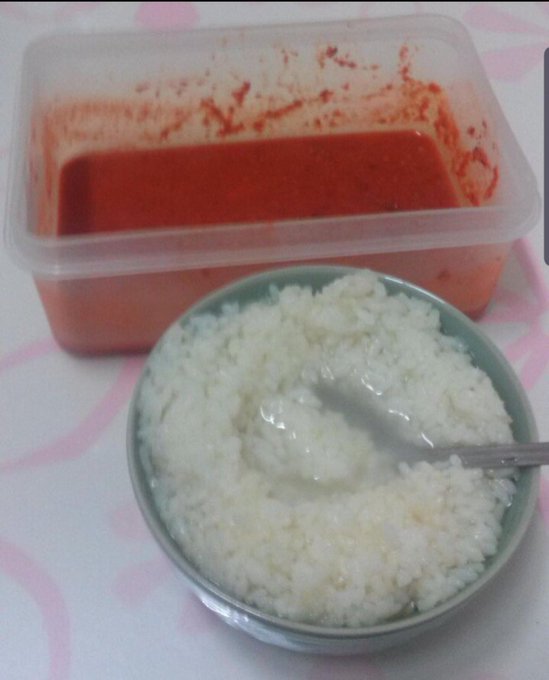 A bowl of white rice with a spoon sits in front of a plastic container of red sauce, possibly a soup or curry, on a patterned tablecloth. The image humorously illustrates the "Plath fans" reference from the post, as the simple meal resembles a basic dish one might find in a modest or humble setting.
