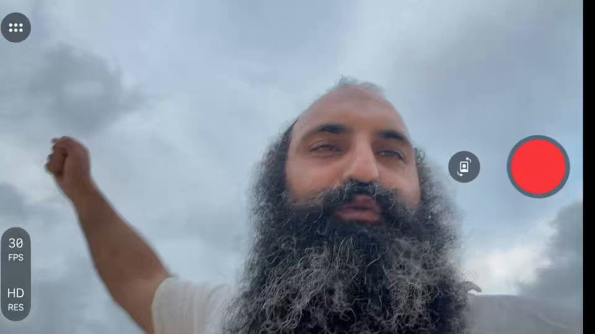 The image features a man with a long beard wearing a white shirt, standing against a cloudy sky. The photo has been edited using a red circle that appears to be a "pop" or "burst," which adds an artistic touch to the scene. The caption of the image reads, "BITCOIN BEAR FLAG TRAP?NVIDIA PUSHES ATH $BTC". This suggests that the man in the picture might have used a photo editing software like Photoshop to create this unique and eye-catching image.