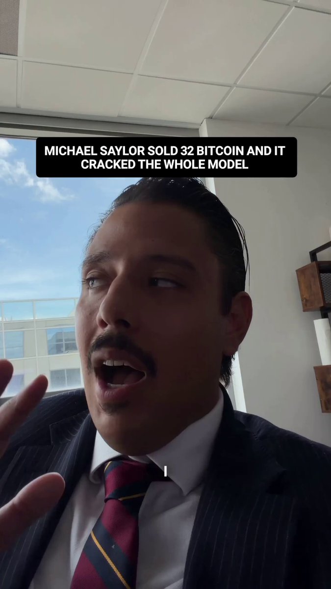 The image features a man dressed in a suit, wearing a red tie with white stripes. He appears to be talking or gesturing while standing next to a window. The caption of the image reads "Michael Saylor Sold 32 Bitcoin and It Cracked the whole Model". This suggests that Michael Saylor sold 32 Bitcoins for the entire model he cracked.