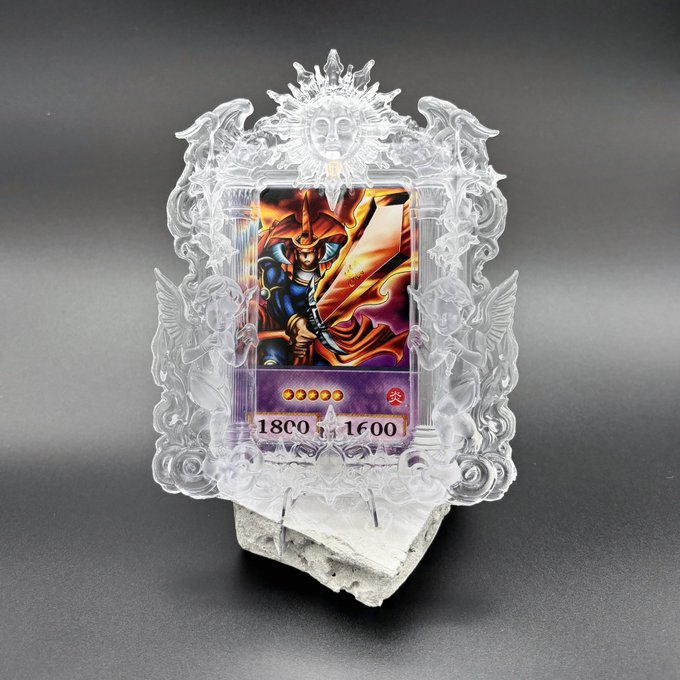 A clear acrylic frame with angel figures at the top and sides holds a Yu-Gi-Oh! card, with stats '1800 ATK/1600 DEF' visible.