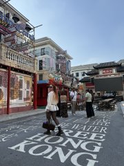 A street view in Hong Kong featuring Chinese signage, pedestrians, and ground text reading "WEATHER PERMITS / HONG KONG".