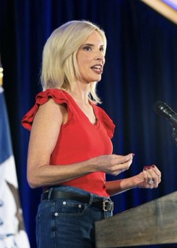 Ashley Hinson speaks at a podium, wearing a red ruffled top and jeans, with no visible text or numbers in the image. The photograph accompanies news of her leading Iowa's Senate race with a 56% chance of winning for the GOP's 6th consecutive Senate victory in the state.
