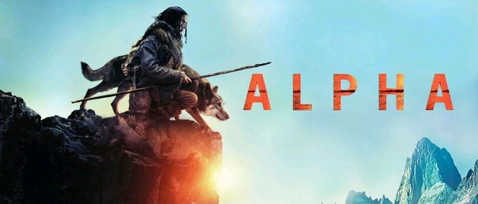 The image features a poster for the movie "Alpha" with an illustration of a man sitting on top of a cliff holding a dog. The background shows a mountain range under a blue sky. The text on the poster reads "ALPHA".