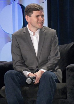 A man in a gray suit jacket and white shirt smiles while seated on a dark couch in what appears to be a studio setting. The image accompanies news that Democrat James Talarico's odds of winning the Texas Senate race have reached an all-time high of 56% on Polymarket.com, likely depicting him during a media appearance.