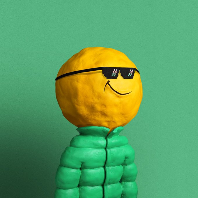Whimsical figure made of sculpted clay or similar material featuring a yellow spherical head with a drawn smile and pixelated sunglasses, and a green puffy body, set against a green background.