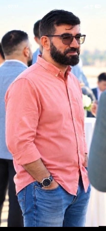 A bearded man wearing glasses, a pink button-up shirt, and jeans stands at an outdoor gathering, with a watch visible on his wrist. The image appears to be a screenshot from a mobile device (timestamp 07:17, with 24 battery remaining) and seems to accompany a post about predicting "Pi's future" based on someone's weight and belly fat.