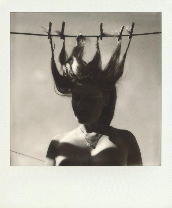 A black and white artistic photograph showing a woman's silhouette as she hangs her hair on a clothesline to dry.