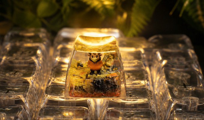 A close-up of an illuminated, transparent resin keycap containing a miniature fox figurine and grass, surrounded by other clear keycaps.