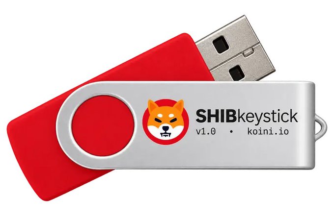 A red and silver USB flash drive featuring the Shiba Inu dog logo with text 'SHIBkeystick v1.0 · koini.io'.