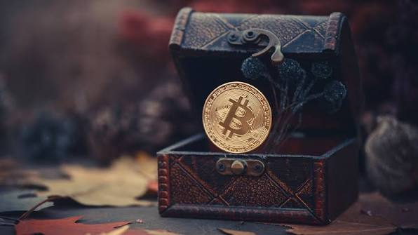 A golden Bitcoin coin rests inside an ornate treasure chest surrounded by autumn leaves, symbolizing the allure of crypto "treasure." The image visually represents the post's theme about the Bitcoin "copy trade" dream, where companies buy Bitcoin hoping to replicate MicroStrategy's success.