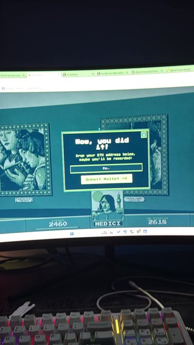 A computer monitor displays a screen reading 'Now, you did it! Drop your ETH address below, maybe you'll be rewarded!' with a 'Submit Wallet' button, shown above a backlit RGB keyboard.