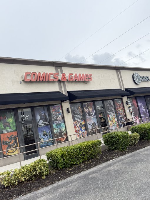 An exterior photograph of a 'COMICS & GAMES' store at address 1402, featuring large window displays filled with comic book covers, located next to 'DR. GRADE'.