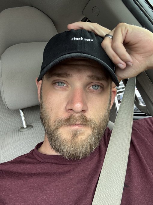 A man wearing a black baseball cap with "stack sats" embroidered on it, reiterates the message of the accompanying post, emphasizing continued dedication to the mission.