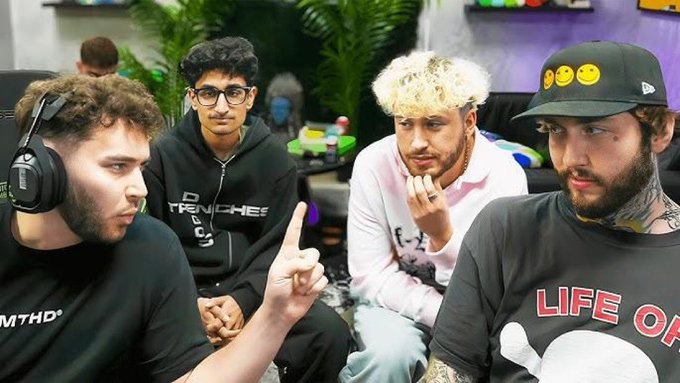 Four young men sit together in what appears to be a casual studio or lounge setting, engaged in conversation. One wears a "TRENCHES" hoodie, another sports a cap with smiley face pins and a "LIFE OF" t-shirt, while the man on the left wears headphones with a "MTHD" logo and points his finger animatedly. The image, posted alongside news about trading terminals surpassing $1 billion in daily volume, likely depicts a crypto/finance content creator group discussing this significant market milestone, with the pointing gesture suggesting they're highlighting or analyzing the achievement.
