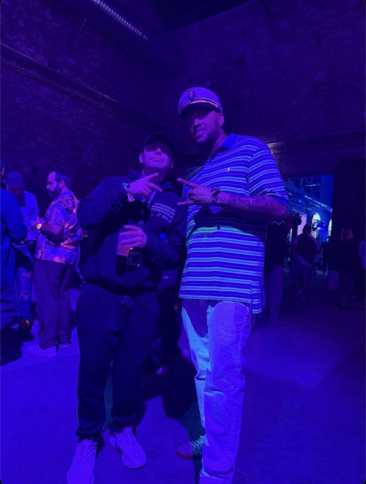 Two friends pose with matching hand gestures at a dimly lit NFT conference bathed in blue lighting, embodying the close-knit "ape fest" atmosphere described in the post.