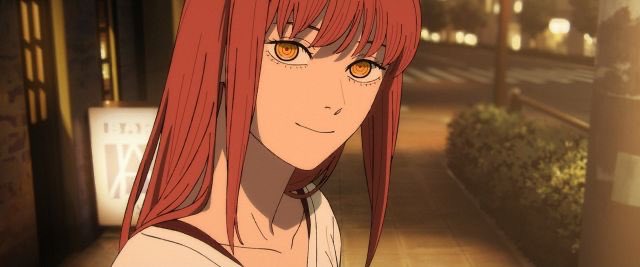 An anime girl with long red hair and striking orange eyes smiles subtly on a city street at dusk. The urban setting, with its illuminated storefronts and sidewalk, connects to the post's theme of choosing between city and country life—suggesting the "city mouse" option.