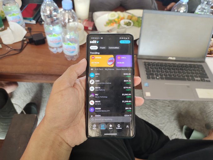 A hand holding a smartphone displaying the SoFi investing app with trending stocks like INTC, AMD, META, and SMCI.