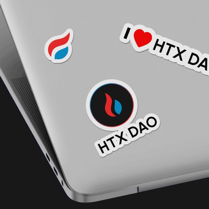 A laptop lid displays three stickers, including two branded with 'HTX DAO' featuring a red and blue flame logo, and one reading 'I ❤ HTX DA'.
