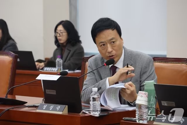 A man in a gray suit speaks into a microphone while holding papers and a pen, with a nameplate reading "정성국" (Jung Sung-guk) visible on the desk. The image relates to the accompanying post as it shows Rep. Jung Sung-guk of the People Power Party, who proposed the bill to postpone virtual asset taxation.