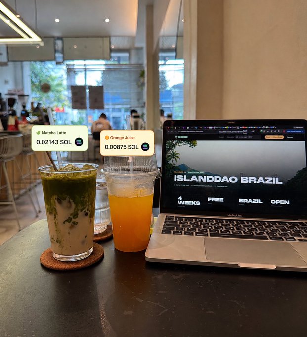 A café scene featuring a matcha latte and orange juice on a table next to a laptop displaying 'ISLANDDAO BRAZIL' website, with cryptocurrency prices overlaid showing Matcha Latte at 0.02143 SOL and Orange Juice at 0.00875 SOL.