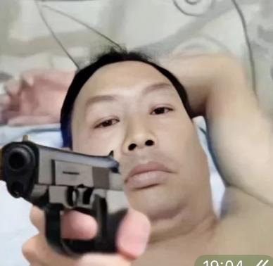A person lying down holding a black handgun pointed toward the camera, with a timestamp '10:04' visible in the corner.