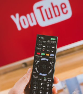 Photograph of a hand holding a Sony TV remote control pointed at a television screen displaying the YouTube logo.