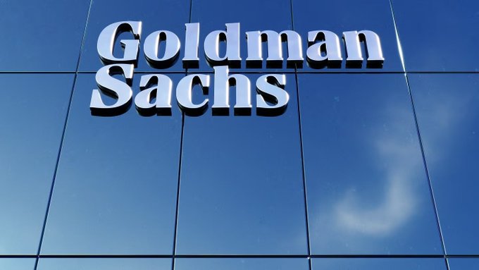 The Goldman Sachs logo displayed in silver lettering on a reflective blue glass building facade.