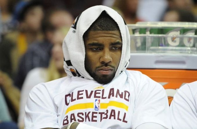 A Cleveland Cavaliers basketball player sits on the bench wearing a white towel over his head and a 'CLEVELAND BASKETBALL' jersey.