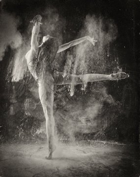The image features a woman with long hair performing an impressive dance move, surrounded by a cloud of dust or powder that appears to be coming out of her mouth. The photo has a vintage appearance, suggesting it might have been taken some time ago. The caption provided in the image reads "Good morning my dear fam happy #TezosTuesday objkt.com/tokens/KT1L3H3 ... #TezosTuesday". This implies that the image is related to a post on Tezos Tuesday and possibly discussing the woman's dance performance or her personal life, as indicated by the caption.