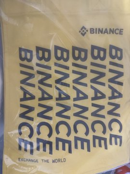 A fan excitedly shows off their new Binance merchandise—a yellow drawstring bag prominently featuring the Binance logo and the slogan "Exchange the World"—thanking the crypto community and Binance for the gift.