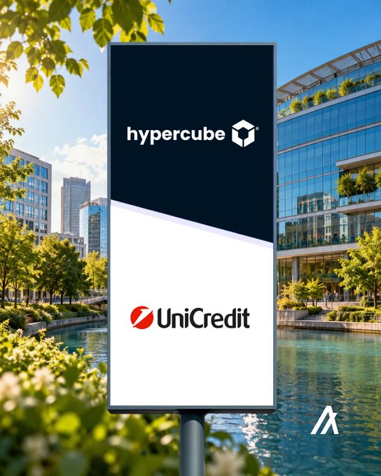 A modern outdoor billboard set against a scenic waterfront and contemporary glass buildings displays the "hypercube" and "UniCredit" logos side by side, visually representing the partnership between the blockchain firm and the major European bank to bring verified water credits to capital markets.