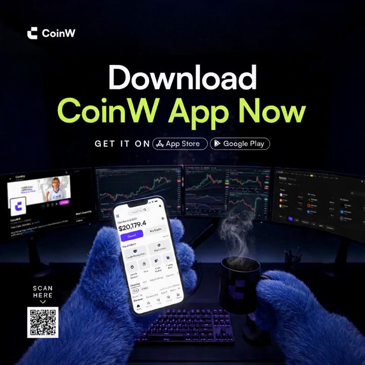 The image shows a person holding up their phone, which has an app for CoinW displayed on its screen. The text "Download CoinW App Now" is visible above the phone. There are also two computer monitors present in the scene, one of which is displaying a graph or chart related to cryptocurrency trading. A cup with a coffee logo can be seen next to the monitor.