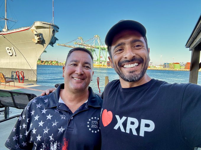Two men pose for a selfie at a waterfront harbor, with one wearing a black "I ❤️ XRP" t-shirt and the other in a star-patterned shirt; in the background, a Navy ship bearing the number "61" and port cranes are visible, complementing the post's tribute to a farewell dinner and gratitude for service.