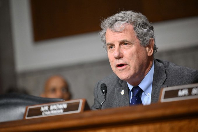 Senator Sherrod Brown, identified by the nameplate, speaks into a microphone during a congressional hearing.