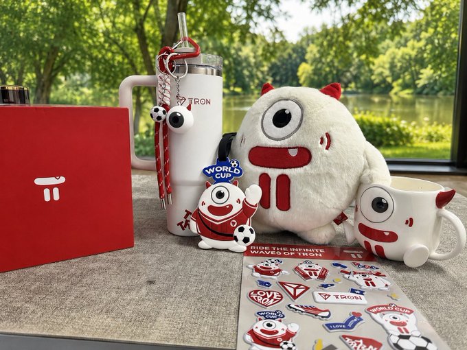 The image showcases a collection of TRON and World Cup merchandise, including a red TRON-branded box, a white tumbler with "TRON" text, a plush mascot toy with one eye and horns, a "World Cup" figurine, an eyeball-themed mug, and a sticker sheet reading "RIDE THE INFINITE WAVES ON BSC." The caption expresses gratitude to @TronDao_VIE for the ambassador gifts, highlighting perks like monthly article rewards, dining experiences, and branded merchandise sent to TRON ambassadors.