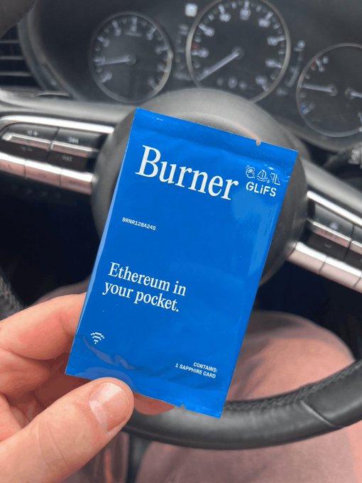 A hand holds a blue "Burner" Glifs packet reading "Ethereum in your pocket" (containing 1 Sapphire card) in front of a car's steering wheel, with the dashboard gauges visible in the background—visually reinforcing the post's "pocket full of ETH" reference.