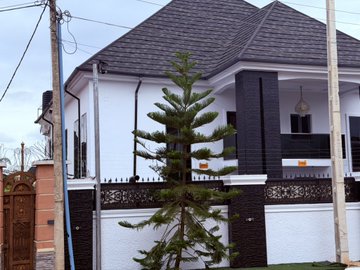 A newly built modern two-story white and black house stands behind a wrought iron gate with a tall pine tree in the front yard, symbolizing the success of completing a fourth home. The caption aligns with the post, celebrating how memecoin profits have funded this latest real estate milestone.