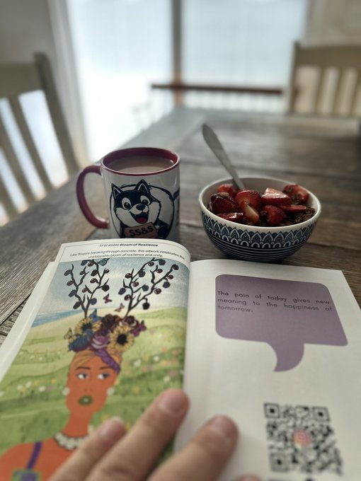 A cozy scene of a person reading an open book about 'The Rose of Resilience' while enjoying a bowl of strawberries and a beverage in a husky-themed mug on a wooden table.