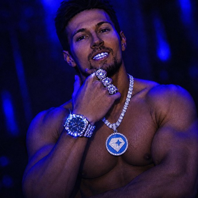 The image features a muscular man with a beard, wearing a diamond necklace and holding a watch over his shoulder. The background of the photo has blue lights that create an interesting visual effect. There are two posts related to the image, one of which is titled "Should I sell all my $Sol to Gram support my Russian husband @durov?". This post seems to be about selling jewelry or other items for a specific purpose, possibly related to supporting someone in Russia.

The man's muscular physique and the presence of the diamond necklace suggest that he might be involved in the jewelry business or is promoting a particular product. The blue lights in the background add an artistic touch to the image, making it visually appealing and drawing attention to the subject matter.