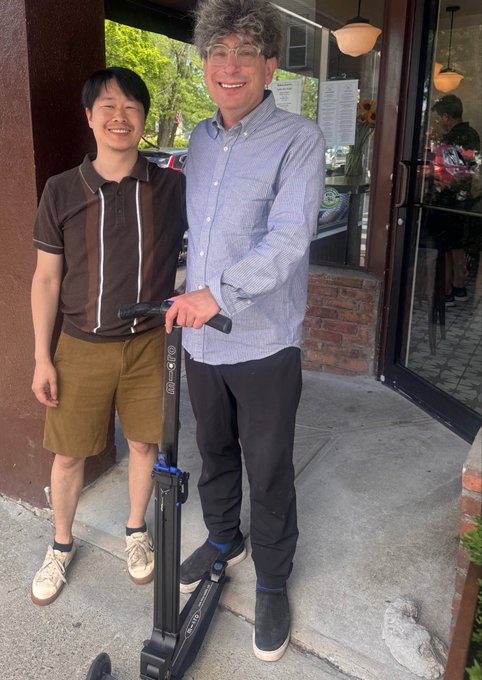 Two men pose on a sidewalk outside a storefront in Hudson, NY—one standing next to an electric scooter (branded "RAZOR" and "E100")—following a chance encounter between the poster and John of @bitsecai, a Bittensor ($TAO) subnet using decentralized AI for cybersecurity.