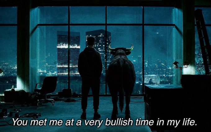 A silhouetted man and a bull stand before large windows overlooking a nighttime cityscape, with the caption "You met me at a very bullish time in my life."