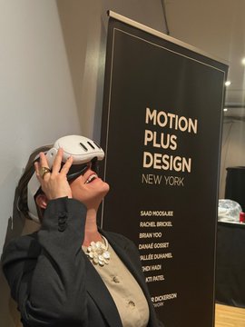 A woman wears a white VR headset while smiling, standing next to a banner reading "MOTION PLUS DESIGN NEW YORK" featuring names like Saqi Nozaki, Rachel Jacob, and David Ariew. The image captures the SUBMERGE VR showcase event, highlighting David Ariew's "Quantum Stargate" among the featured works.