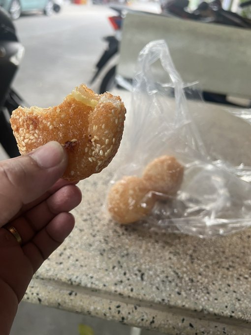 A close-up photo shows a hand holding a partially eaten sesame seed bun with yellow filling, with more buns visible in a clear plastic bag in the background.
