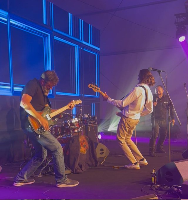 The image features a band performing at an event with a stage set up. The lead singer of the band is playing a guitar while another member stands next to him, holding a microphone. A third person can be seen standing behind them on the stage. The background includes a blue wall and purple lights, creating a vibrant atmosphere for the performance.

The image also contains text that reads: "Thank you @kucharmartin_ & @Matyas44Cook & team for another amazing @BTCPrague event! To those that haven'nt ever been to a Bitcoin event yet - what are you waiting for, you cowards? And to those that have, but aren't supporting BIP110 yet - what are you waiting for, you cowards?". This message seems to be related to the band's performance and highlights their involvement in the Bitcoin community.