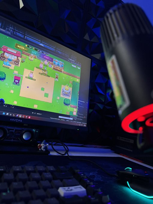 A gaming setup featuring an 'ARZOPA' monitor displaying a colorful game, accompanied by a microphone, keyboard, and RGB lighting against a geometric blue wall.