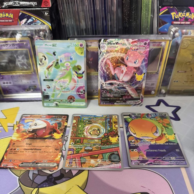 A collection of Pokémon Trading Card Game cards from the 151 set is displayed, featuring standout pulls including a 160 HP Mewtwo ex, a 310 HP Mew VMAX (the "Tag Team" variant), Fuecoco ex (210 HP), Orthworm ex, and a green-colored card. The cards are laid out on a colorful Pokémon-themed playmat, with booster boxes visible in the background, perfectly capturing the excitement of opening a new set and pulling rare "bangers."