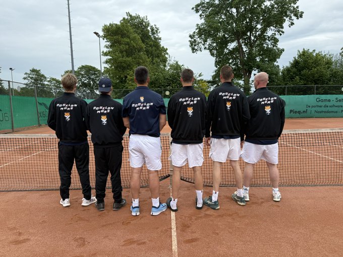 The image features a group of five men standing together, all wearing black shirts with white text that reads "Team Dogelon Mars!". They are positioned on a tennis court, which has a net dividing them into two teams. The players appear to be posing for a photo or waiting for their turn in the game.