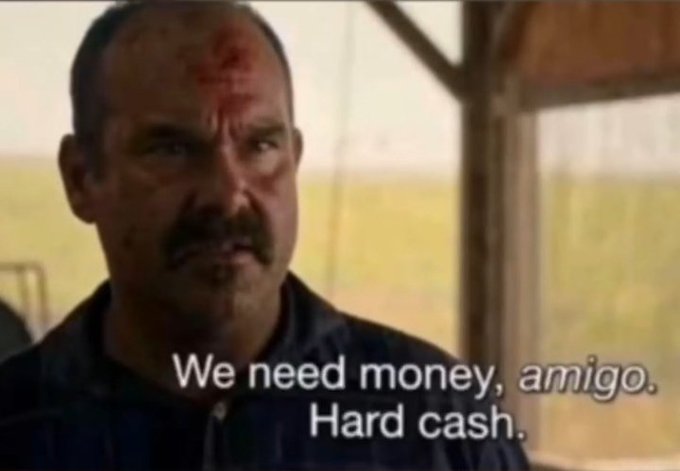 A meme screenshot from a movie showing a man with a mustache and a bleeding forehead wound, captioned 'We need money, amigo. Hard cash.'