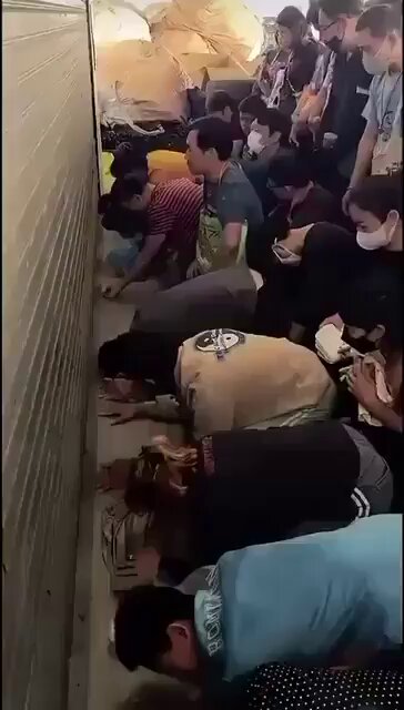 The image shows a group of people kneeling or lying down, with some holding bags as they pray. They are gathered around a wall that has a sign attached to it, which reads "ZEC holders trying to dump their bags before it finally hits ZERO". The people appear to be in the process of emptying their belongings onto the ground, possibly preparing for an evacuation or a similar event.
